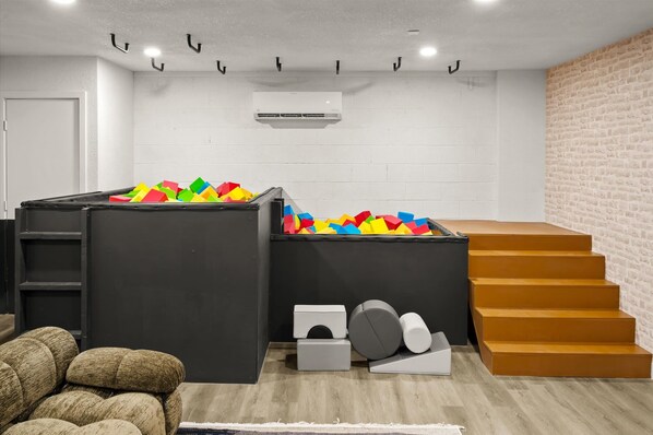 A room with a play area, a staircase, and a white brick wall. - Rock Climbing Wall~Pool& Mini Golf~Game Room~Mural (Peoria)