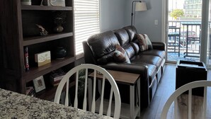 Una sala de estar con un sofá de cuero marrón oscuro, una silla blanca, una mesa de mármol, una estantería y un ventilador de techo.