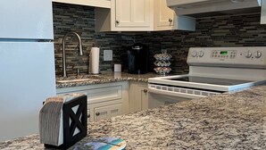 Una cocina con gabinetes blancos, encimera de granito, cafetera y estufa.