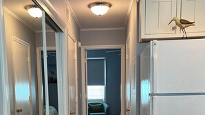Un pasillo estrecho con suelo de madera, armarios blancos y un refrigerador blanco.