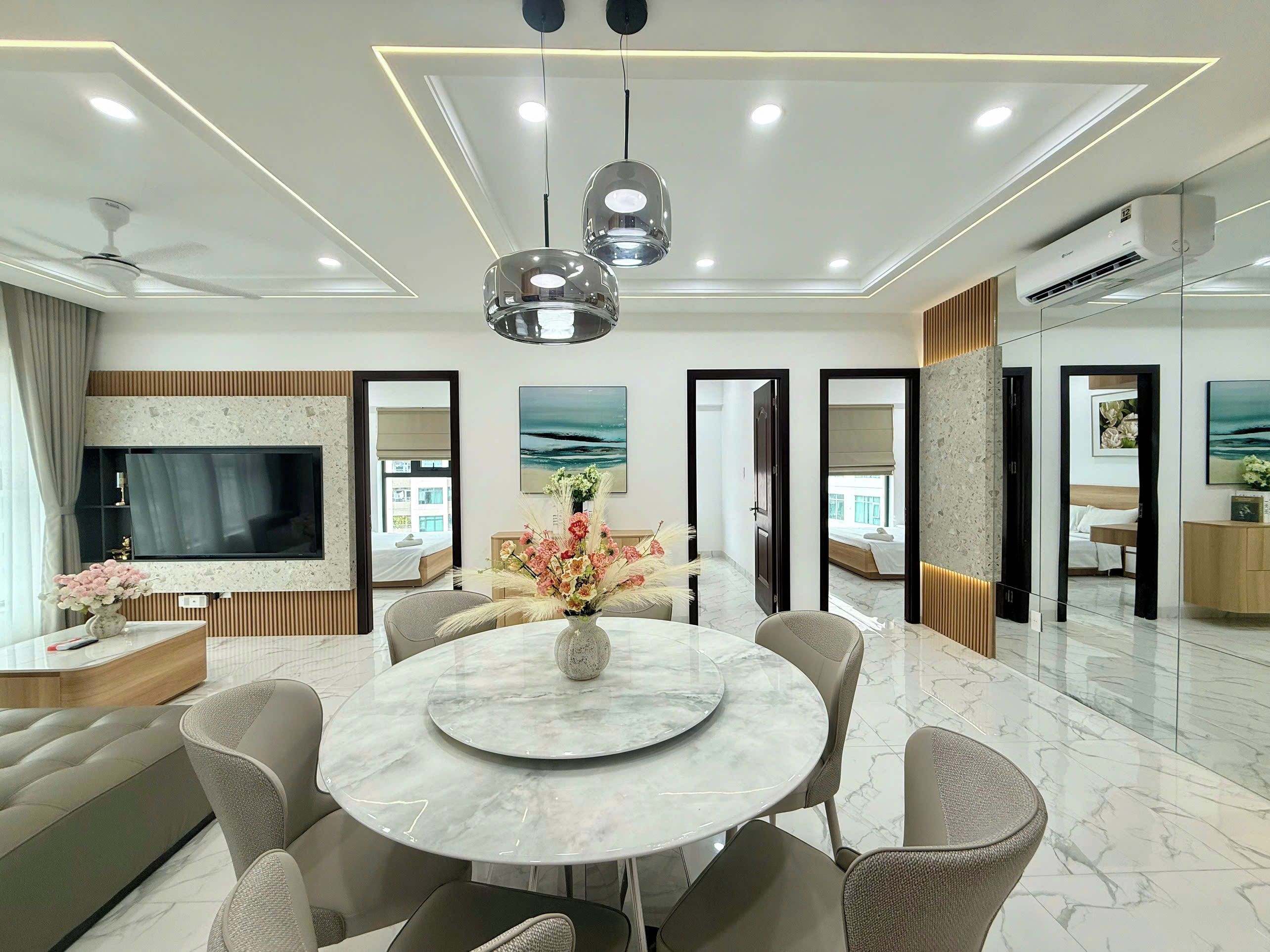 A modern hotel room with a marble dining table, comfortable seating, a flat-screen TV, and artwork on the walls.