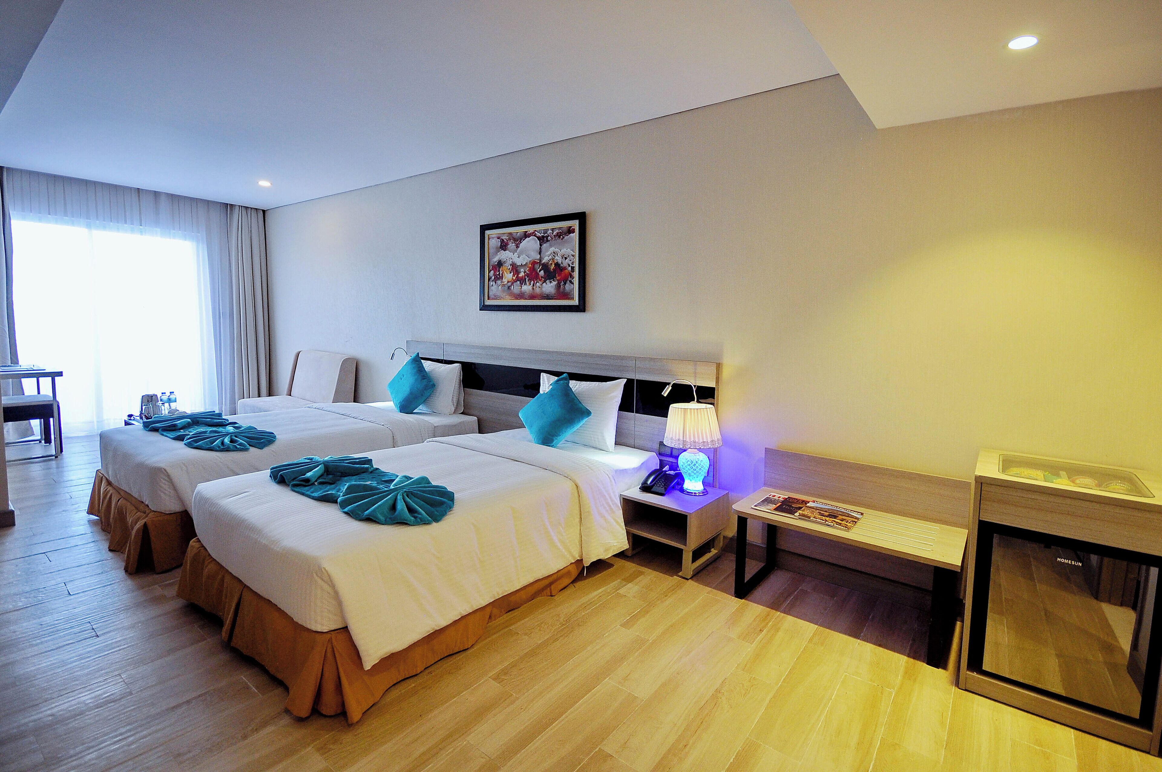 Ein Hotelzimmer mit zwei Betten, einem Nachttisch mit Lampe, einem kleinen Fernseher und einem Fenster mit Vorhängen.