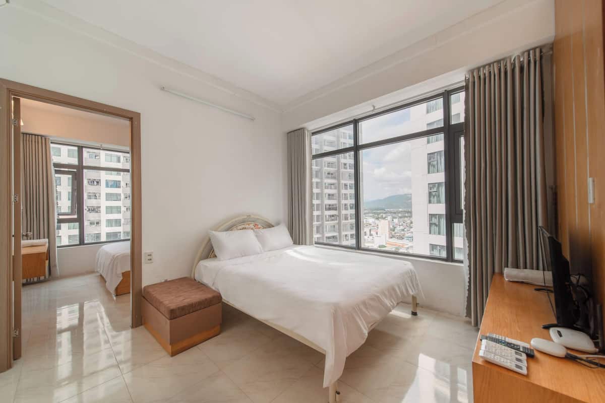 A hotel room with a bed, a desk with a computer, a chair, and a window with curtains.