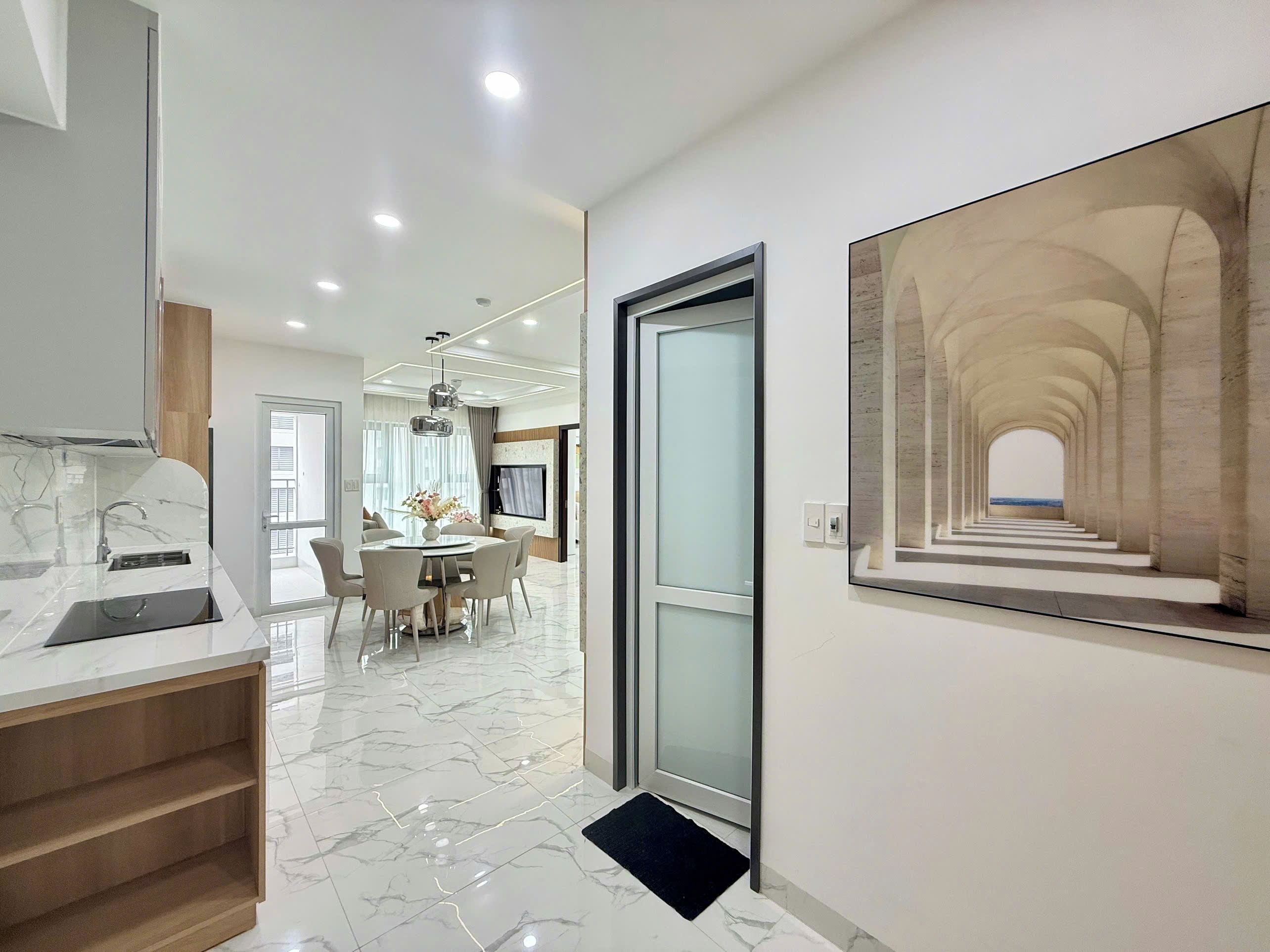 A modern interior with a kitchen, dining area, and a hallway leading to a living space.