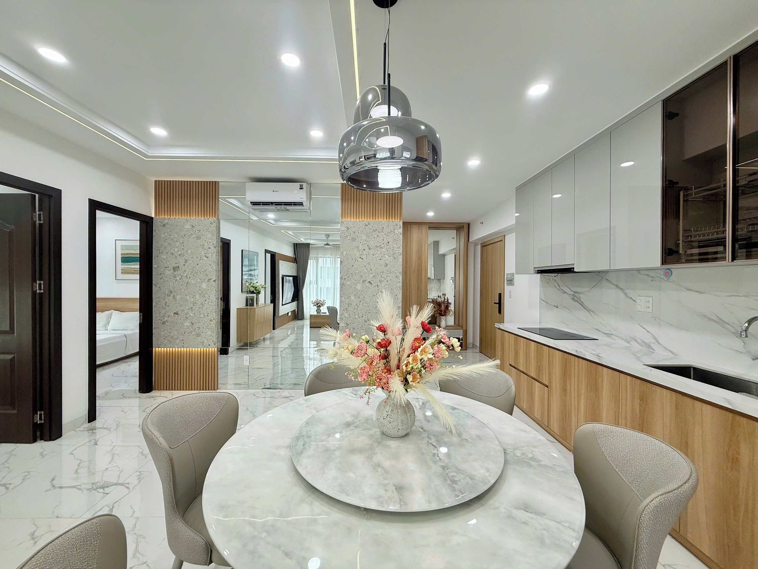A modern kitchen with marble countertops, a round dining table with chairs, and a pendant light.