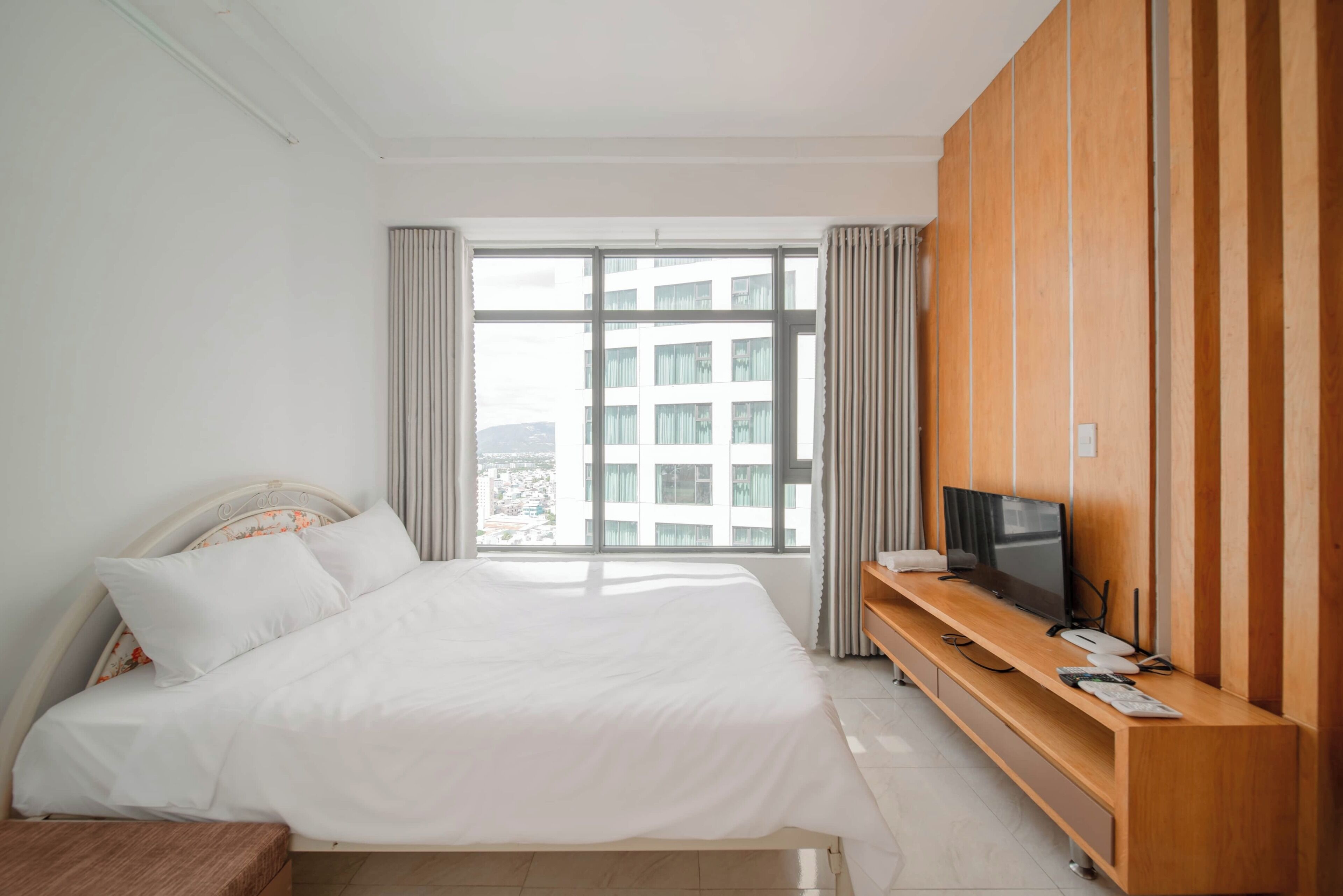 A hotel room with a large bed, a TV on a wooden console, and a window with curtains.