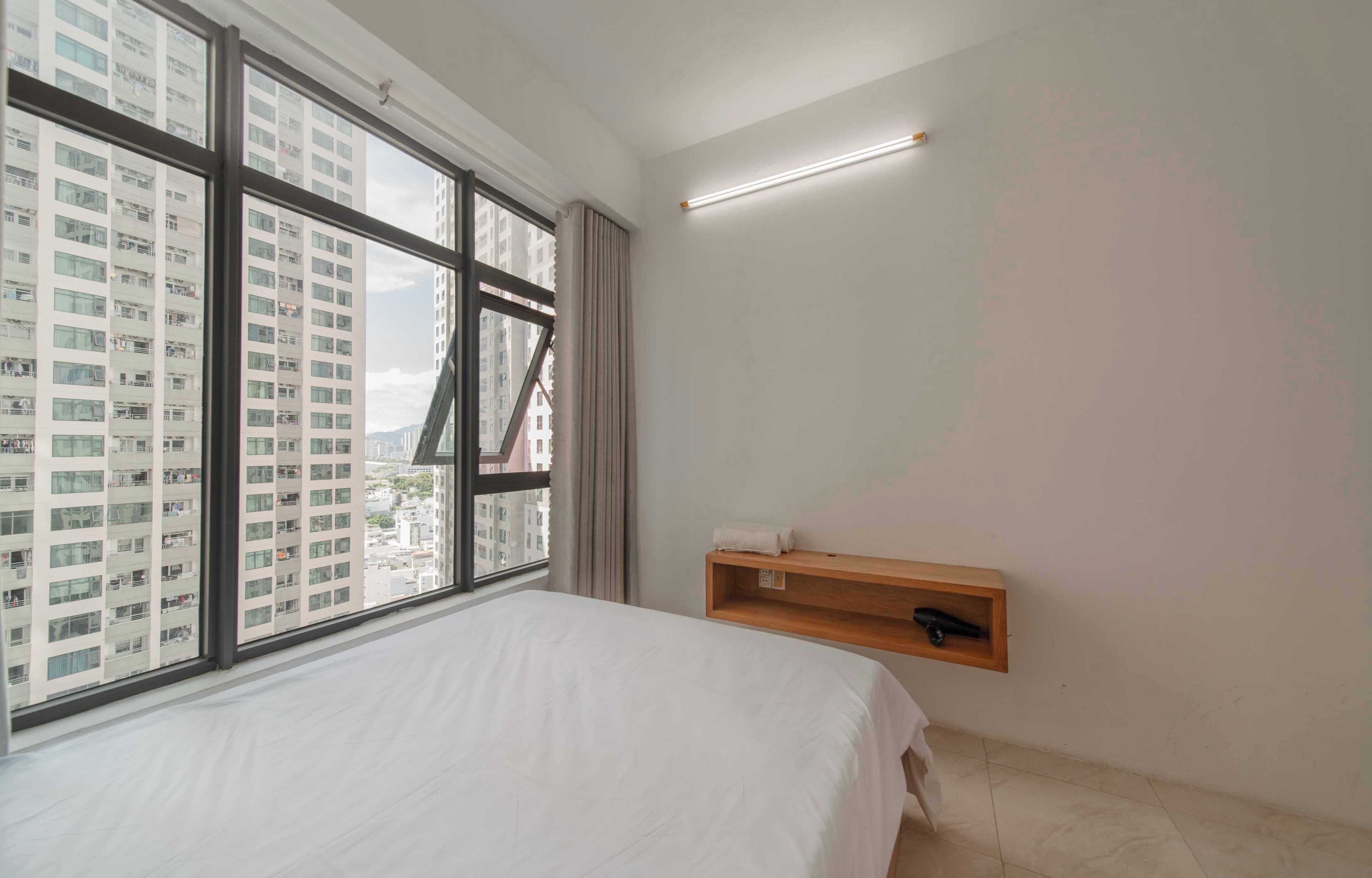 Un dormitorio con una ventana grande, una cama, un estante de madera y una lámpara en el techo.