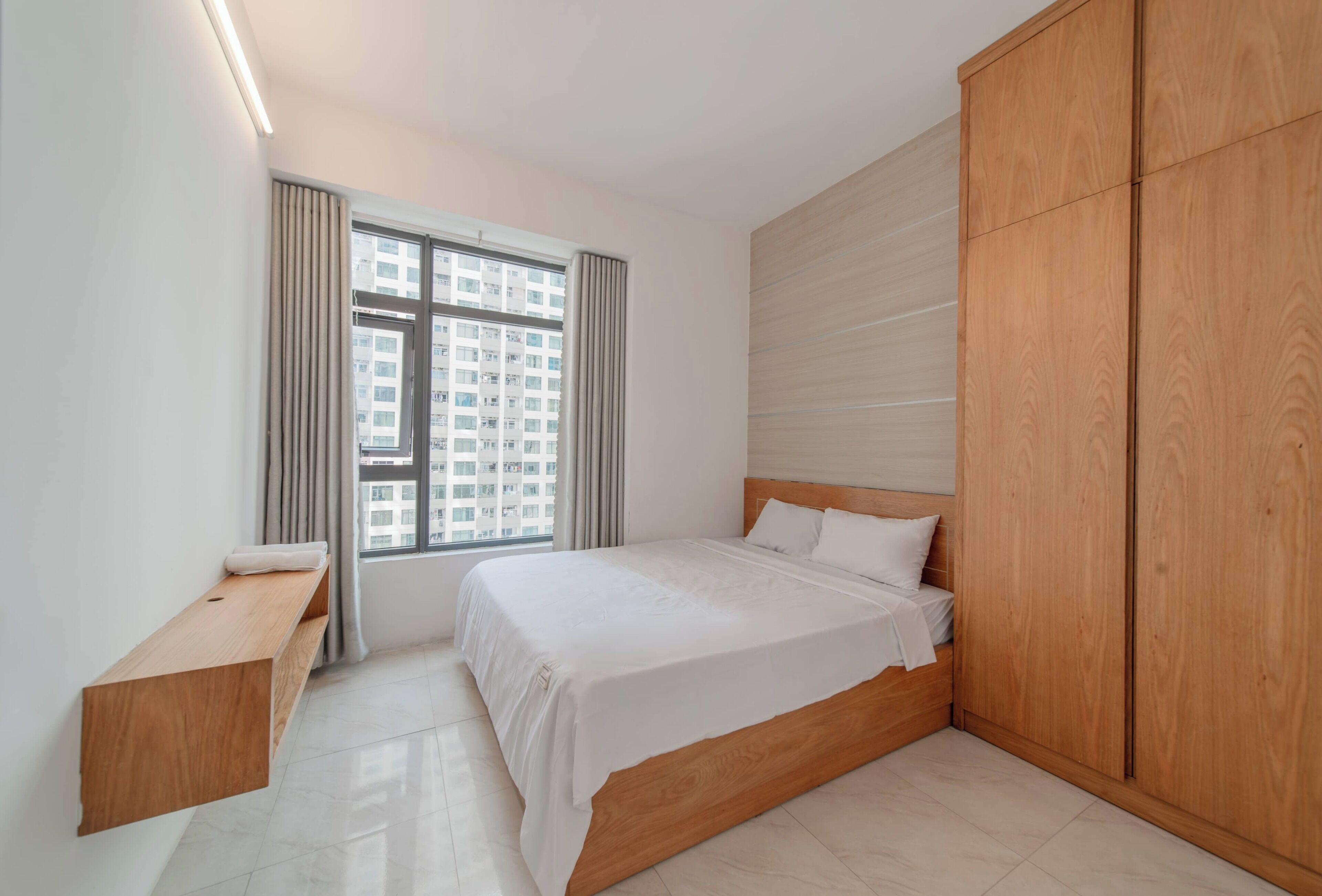 A modern bedroom with a large bed, wooden wardrobe, and a bedside table.