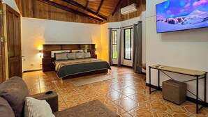 A spacious room with a large bed, a sofa, and a television mounted on the wall. - La Casa de Piedra: Un Hogar Único (Puerto Jiménez)