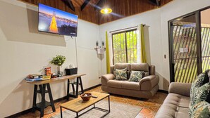 A cozy living room with a wooden ceiling, a television mounted on the wall, a sofa, a coffee table, and a dining area with a table and chairs. - La Casa de Piedra: Un Hogar Único (Puerto Jiménez)