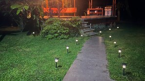 A covered outdoor area with a stage and seating, surrounded by well-maintained grass and plants. - La Casa de Piedra: Un Hogar Único (Puerto Jiménez)
