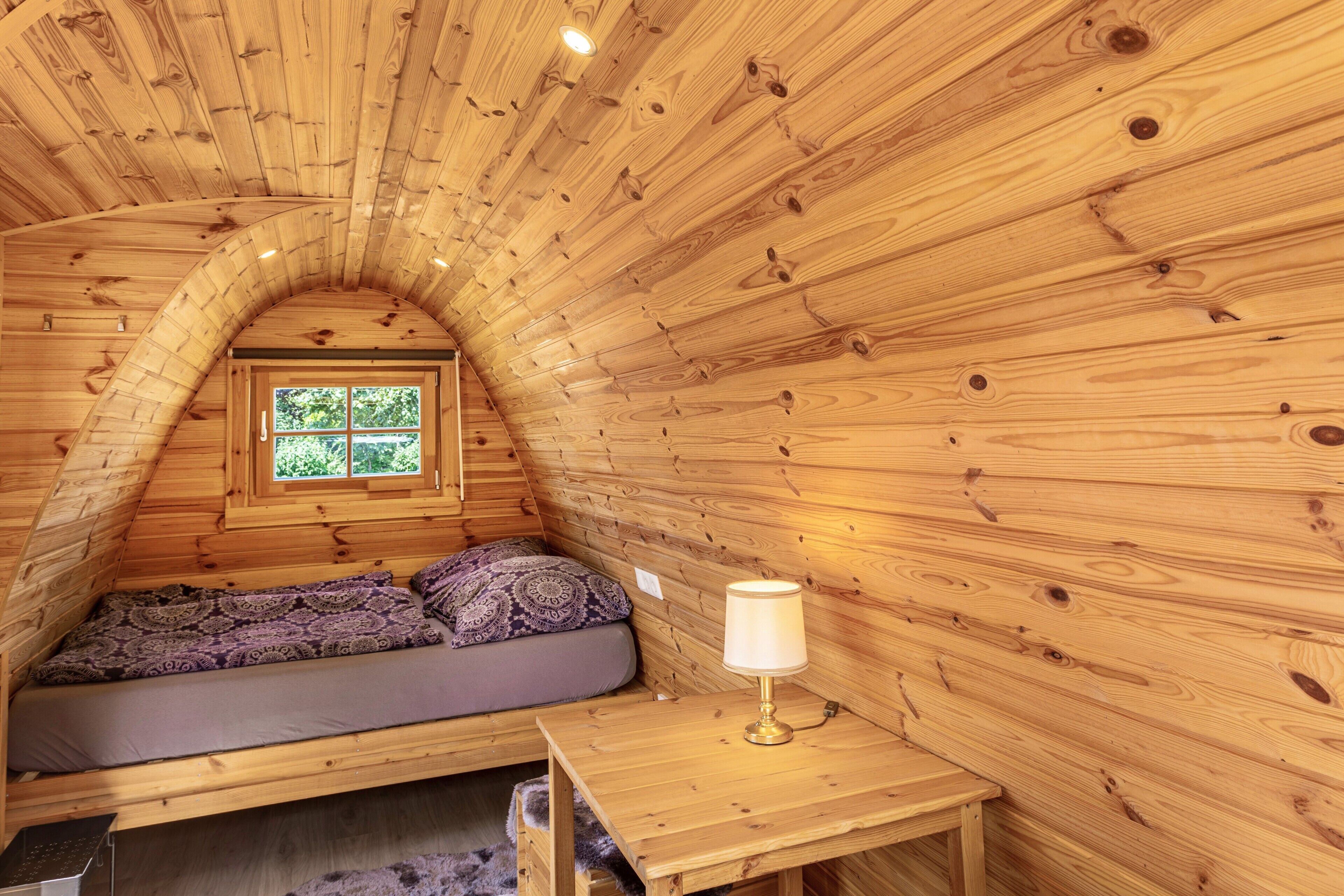 Een knus houten huisje met een slaapzolder, een tafeltje en een raam.