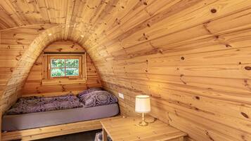 Une cabane en bois chaleureuse, avec un lit en mezzanine, une petite table et une fenêtre.