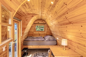 A cozy attic bedroom with a sloped ceiling, a bed, a small table, and a window.
