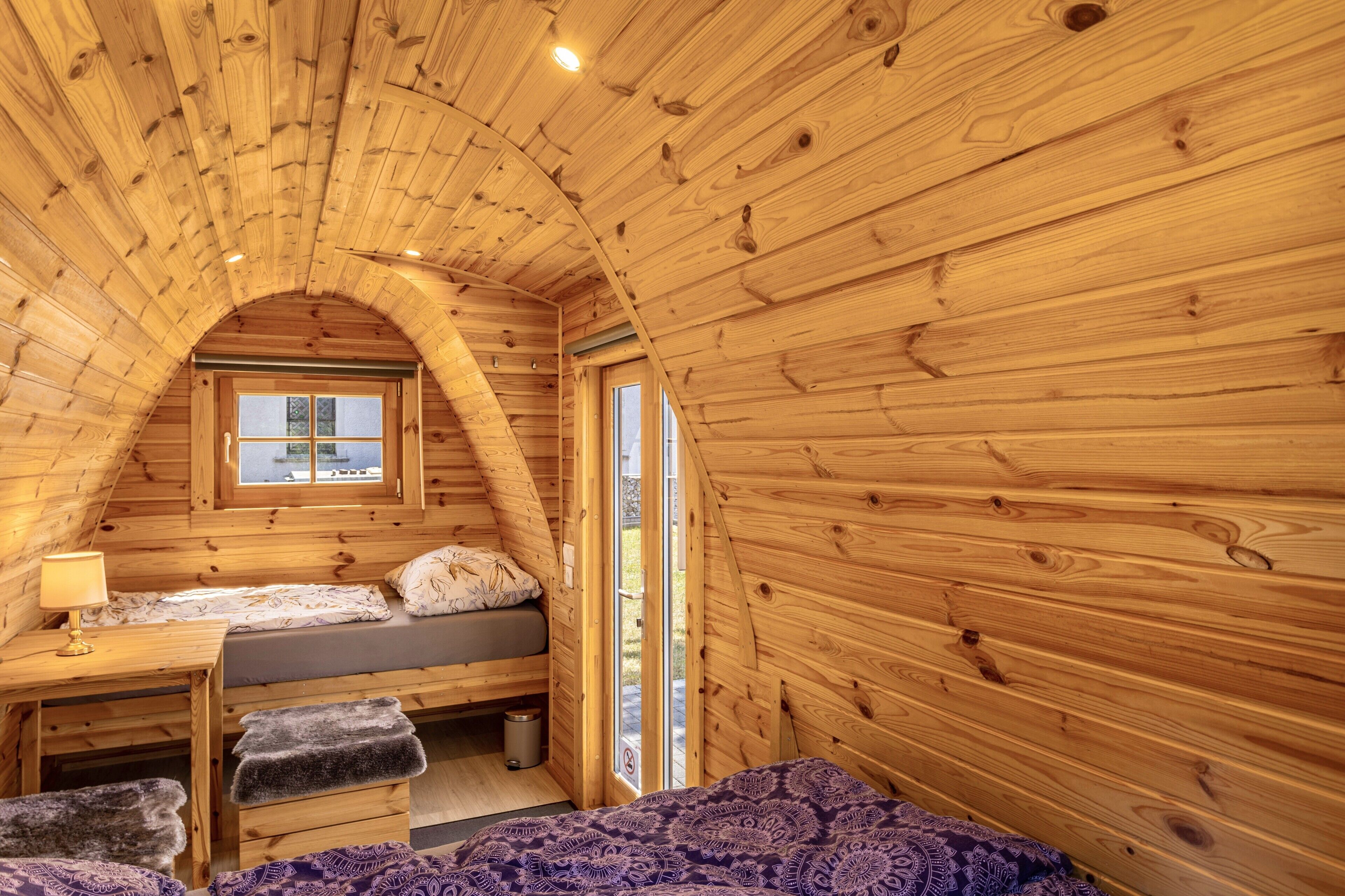 Een gezellig vakantiehuisje met schuine daklijn, een bed met raam, een bureau en een bank.