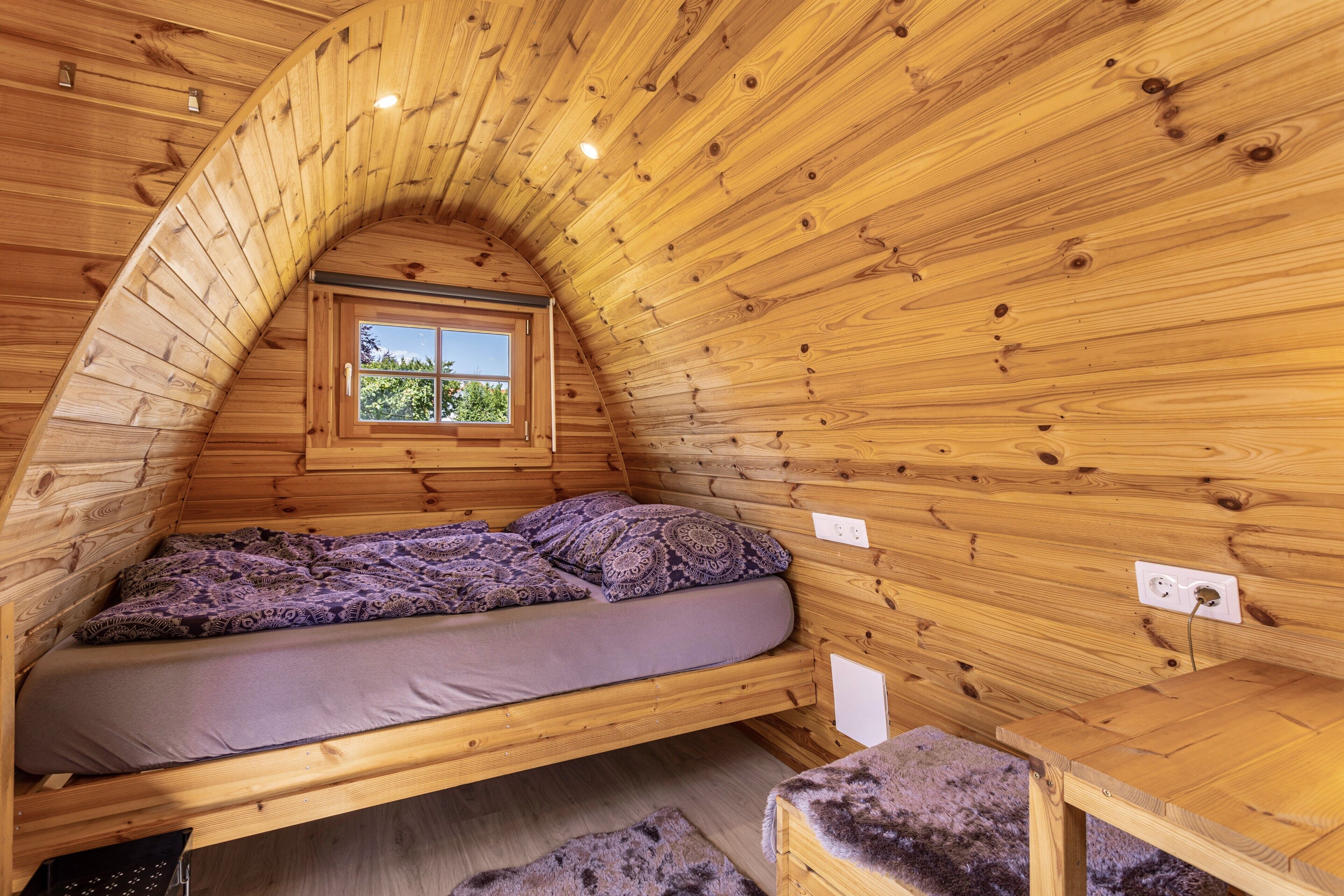 Un interior de madera con una cama, una ventana y una mesita.