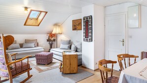 A cozy room with a sofa, rocking chair, wooden side table, and a dining area with chairs and a table. - Apartment 'Ferienwohnung Haus Greif' with Mountain View, Balcony and Wi-Fi (Garmisch-Partenkirchen)
