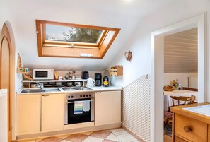 A compact kitchen with a skylight, a microwave, stove, oven, and a small dining area with a table and chair.