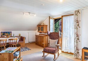 A cozy room with a dining table, chairs, a rocking chair, a wooden cabinet, and a window with curtains.