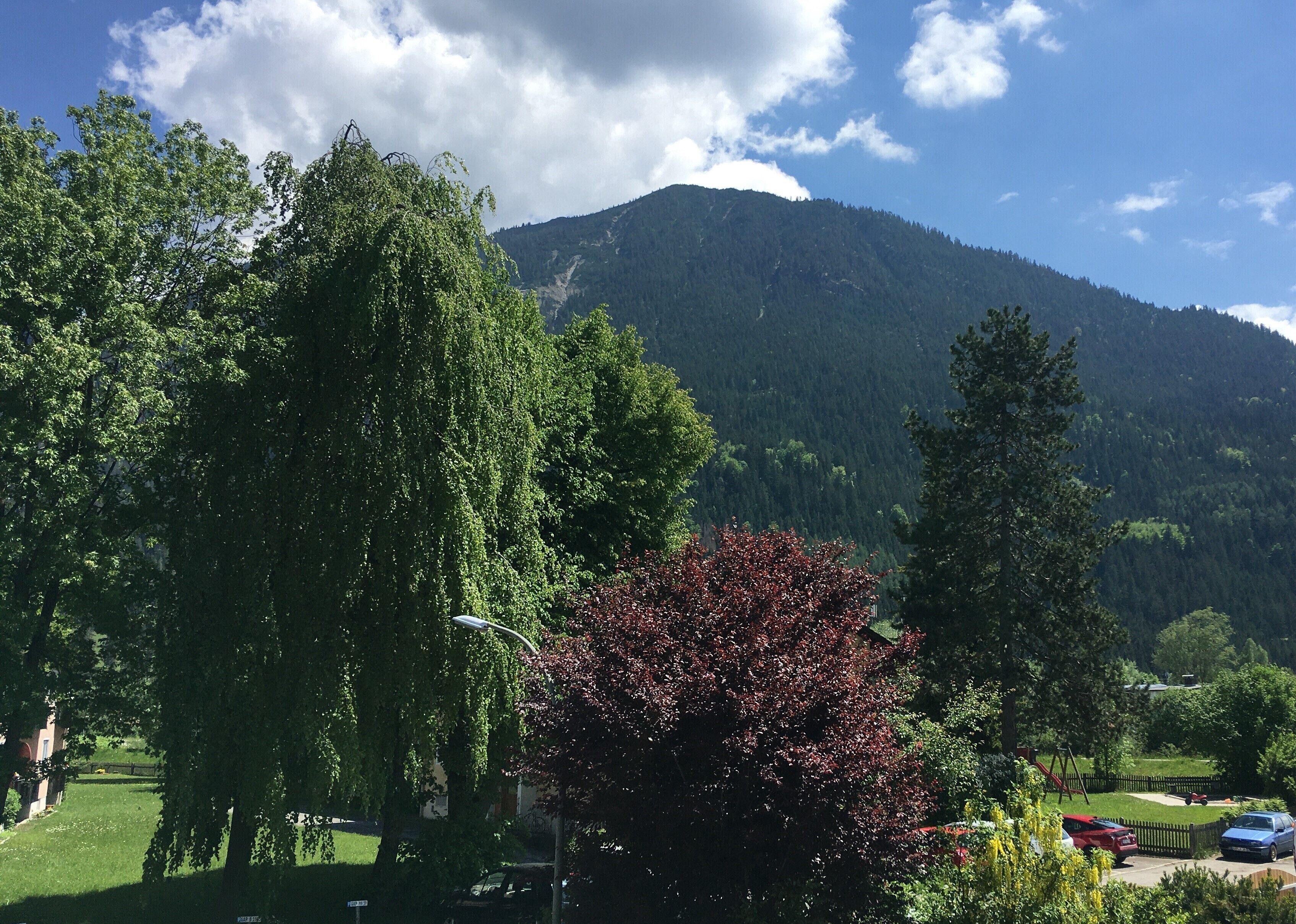 A mountainous landscape with a clear sky, trees, and a playground.