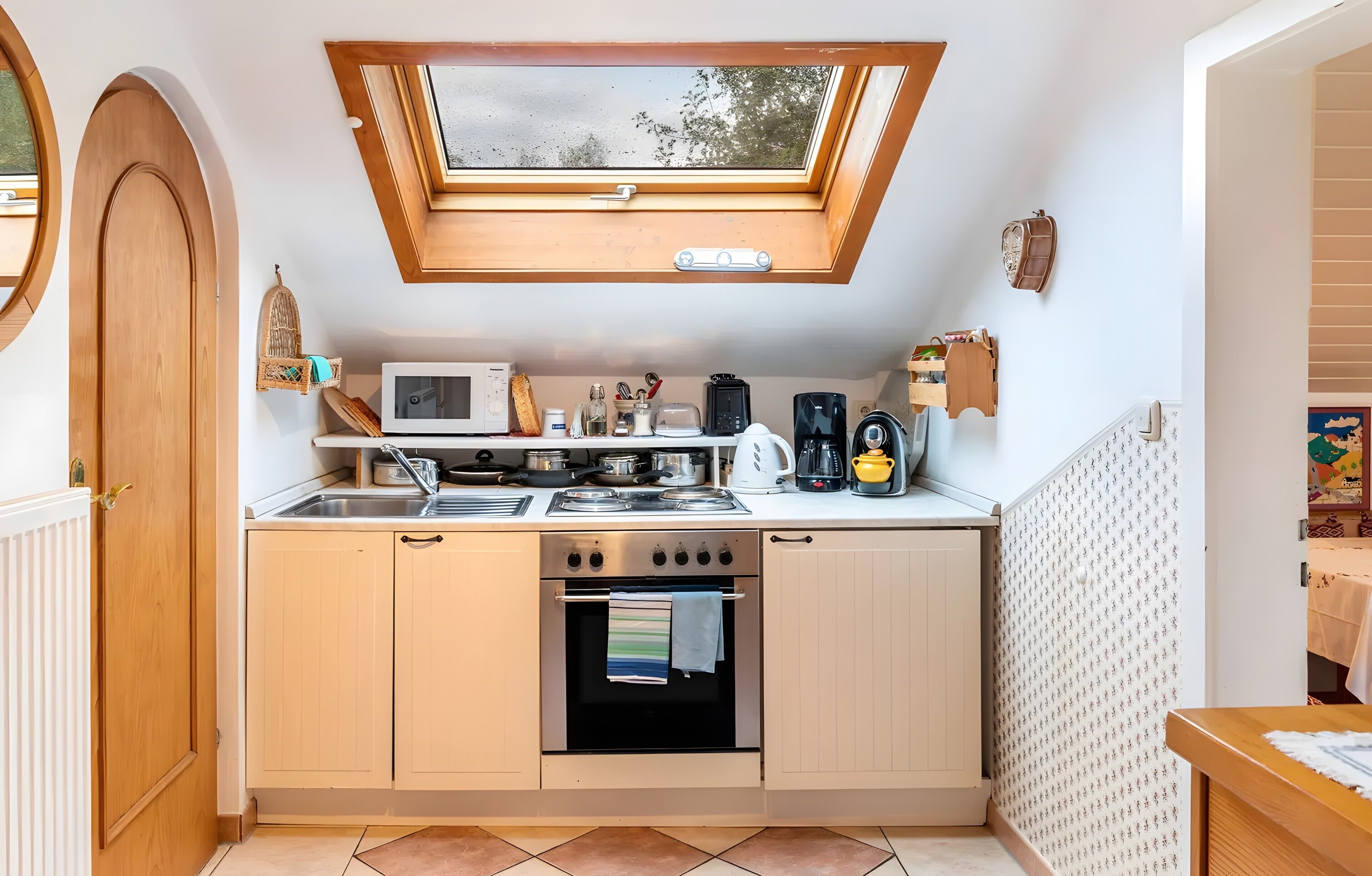 A compact kitchen with a skylight, a microwave, a stove, and a coffee maker.