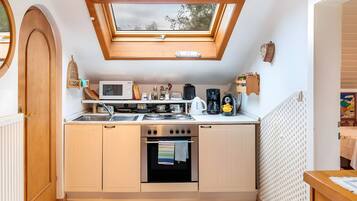 A compact kitchen with a skylight, a microwave, a stove, and a coffee maker.