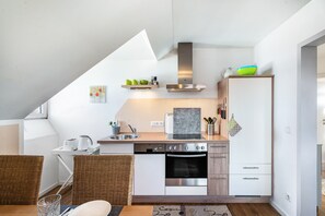 Een moderne keuken met een ingebouwde oven, een magnetron en een roestvrijstalen afzuigkap. Er is een eethoek met rieten stoelen en een tafel.