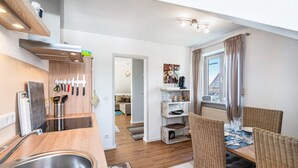 A modern kitchen with a stainless steel sink, wooden cabinets, and a dining area with wicker chairs and a table set for four. - Apartment 'Ferienwohnung Hobmaier' with Mountain View, Shared Garden and Wi-Fi (Forstern)