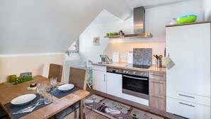 A modern kitchen with a dining area, including a wooden table set with plates and glasses, a built-in oven, and a stainless steel sink. - Apartment 'Ferienwohnung Hobmaier' with Mountain View, Shared Garden and Wi-Fi (Forstern)