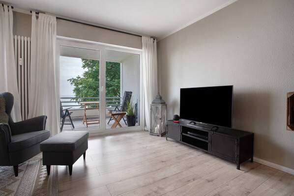A living room with a sofa, ottoman, TV, and a sliding glass door leading to an outdoor area with a table and chairs.