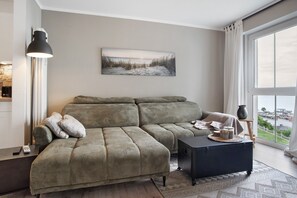 A modern living room with a sectional sofa, a black ottoman, a floor lamp, and a large window with a view.