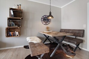A room with a wooden bookshelf, a round wall clock, a table with woven placemats, a bench, and a fur throw.