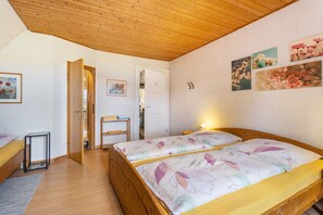 A bedroom with two beds, wooden flooring, a wooden ceiling, and a door leading to another room.