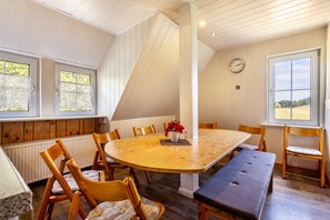 A dining area with a large wooden table, chairs, a bench, and a clock on the wall.