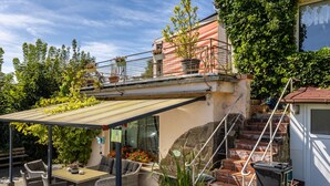 A covered patio with wicker furniture, a staircase, and potted plants.