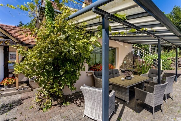 A covered outdoor seating area with wicker furniture, a table, and a pergola structure.