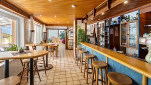A restaurant with wooden tables and stools, a bar area with shelves of bottles, and a view through the windows.