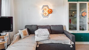 Una sala de estar moderna con un sofá, un televisor de pantalla plana, una lámpara decorativa y un aparador con puerta de cristal.
