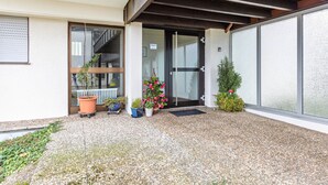 Entrada de un edificio con puerta de vidrio, plantas en macetas y una pequeña escalera visible a través de la puerta.
