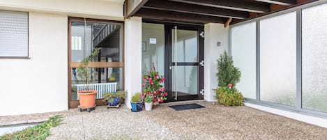 A building entrance with a glass door, potted plants, and a small staircase visible through the door.