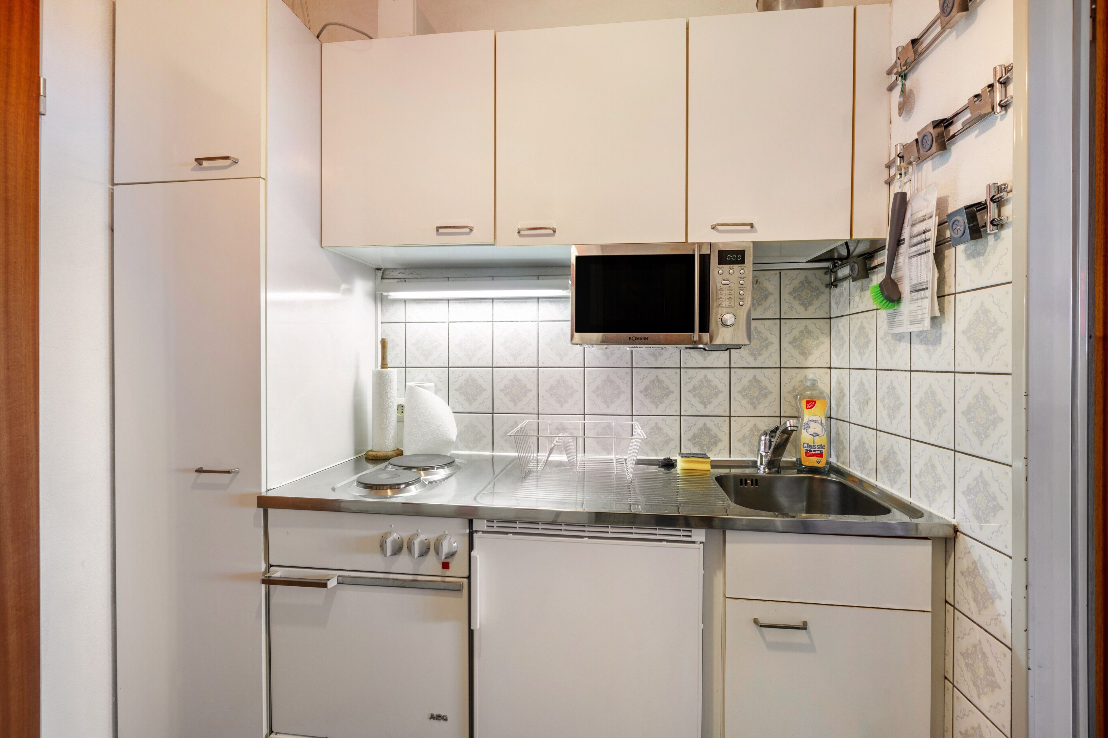 Une cuisine compacte avec des meubles blancs, un four à micro-ondes, un évier et un égouttoir à vaisselle.