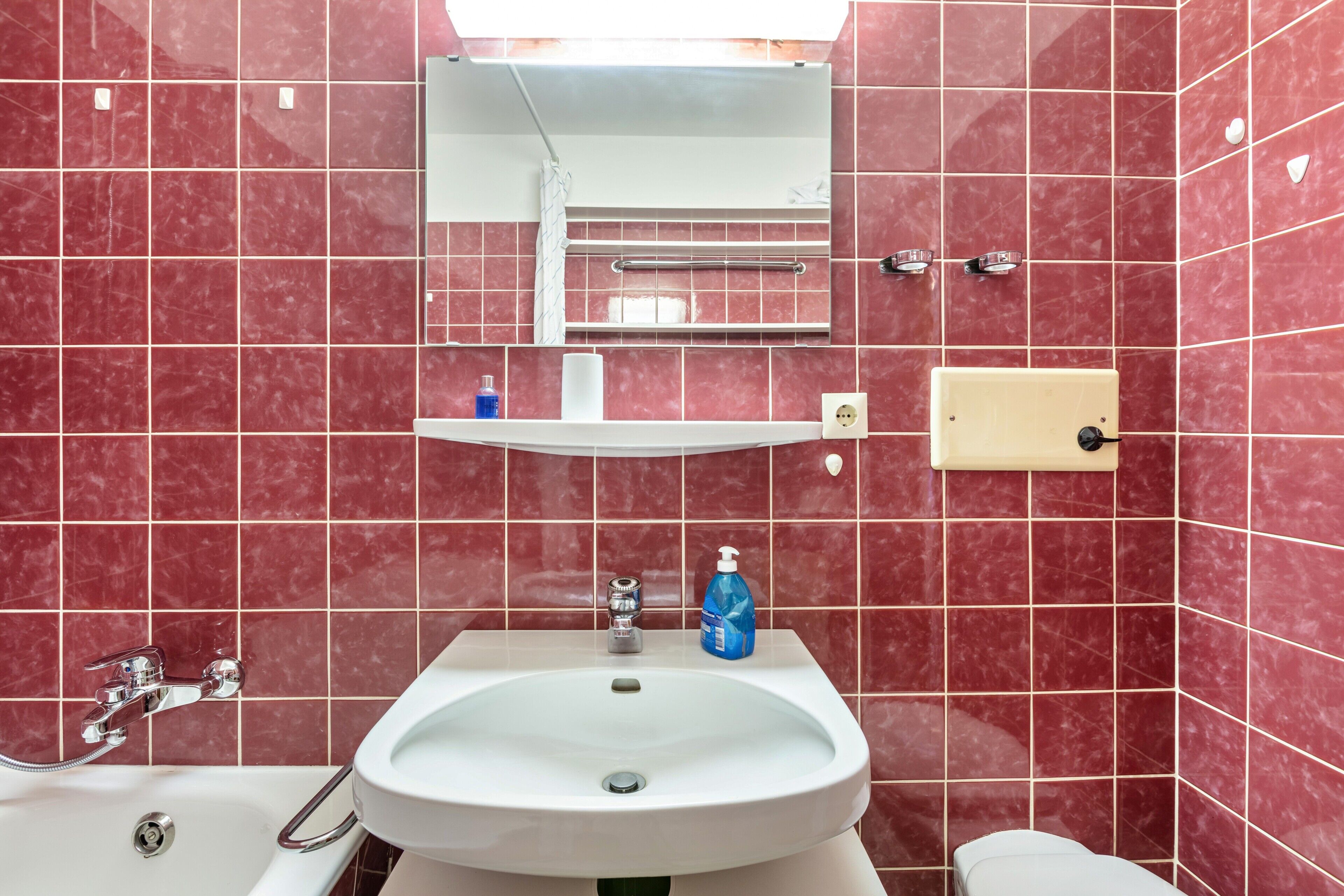 Une salle de bain avec un lavabo blanc, un miroir et des murs recouverts de carreaux rouges.