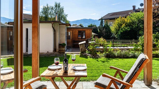 Een houten pergola met een tafel gedekt voor twee personen, met uitzicht op een weelderige tuin en een bergpanorama.