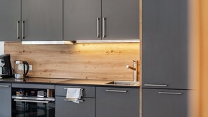 Een moderne keuken met grijze kastjes, een houten spatwand, een inbouwoven en een koffiezetapparaat.