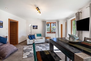 A modern living room with a sofa, a dining table, a TV, and a window with curtains.