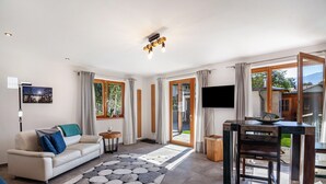 Een moderne woonkamer met een bank, salontafel, televisie en een eethoek met een tafel en stoelen.