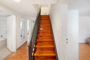 A staircase with wooden steps and a metal railing, leading to a room with white walls and a door.