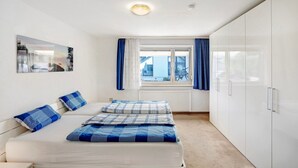 A bedroom with a bed, a window with curtains, a radiator, and a wardrobe.