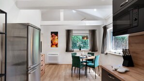 A modern kitchen with a stainless steel refrigerator, a dining table with chairs, a window with a view of greenery, and a microwave. - "Antilope" Apartment in Würmtal with Terrace, Wi-Fi, and Air Conditioning (Gräfelfing)