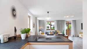 A modern kitchen with a central island, a dining area with a view, and a living space with a sofa and a coffee table. - Falkenstein Apartment with Mountain View, Two Balconies, Private Sauna (Garmisch-Partenkirchen)
